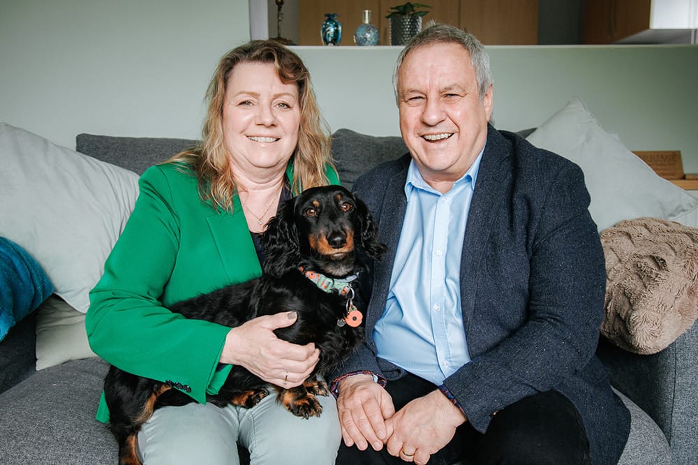Guardianship-Image-1 Simon and Linda sitting on a sofa with a dog between them.